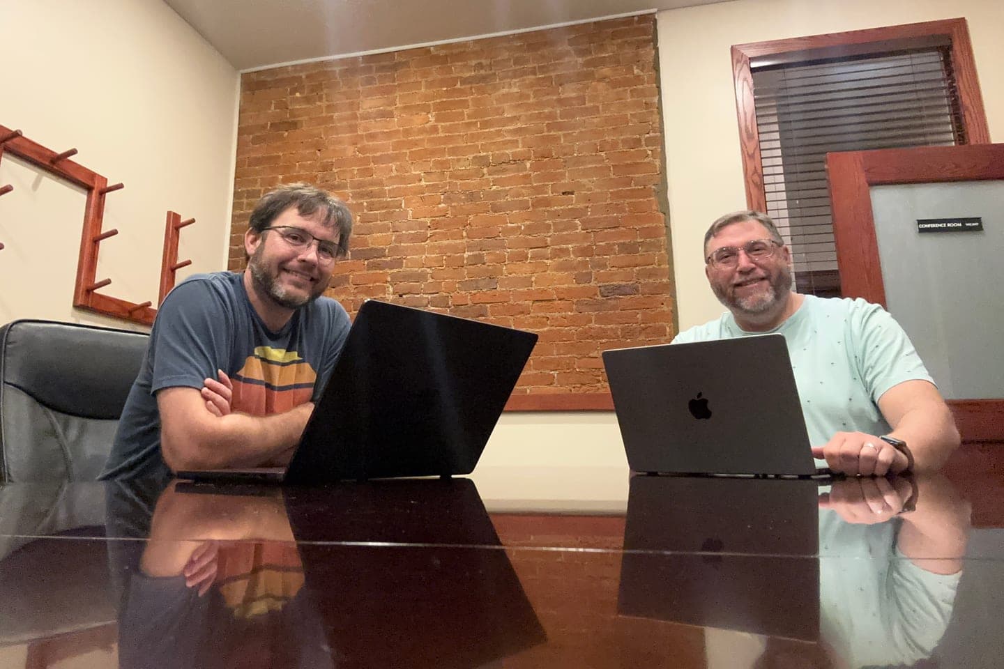 NobleCloak founders David McNelis (left) and Aaron Nicely (right) at a conference table with laptops.